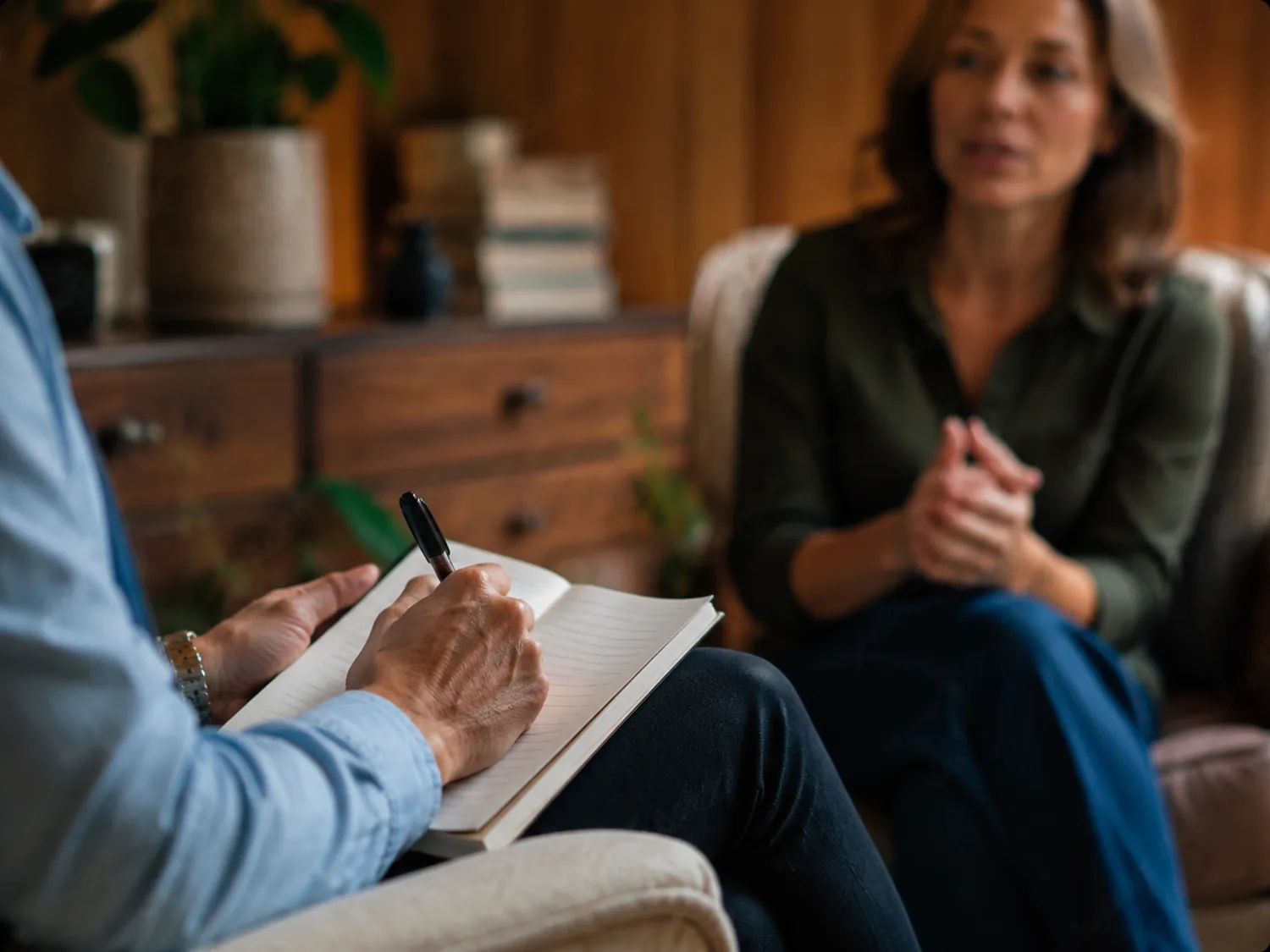 Psicoterapeuta tomando notas en su libreta mientras escucha a una paciente en consulta